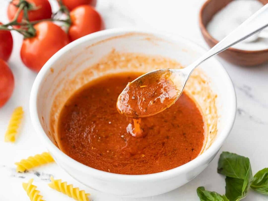 Side view of a bowl of tomato basil vinaigrette with a spoon dripping the dressing into a bowl