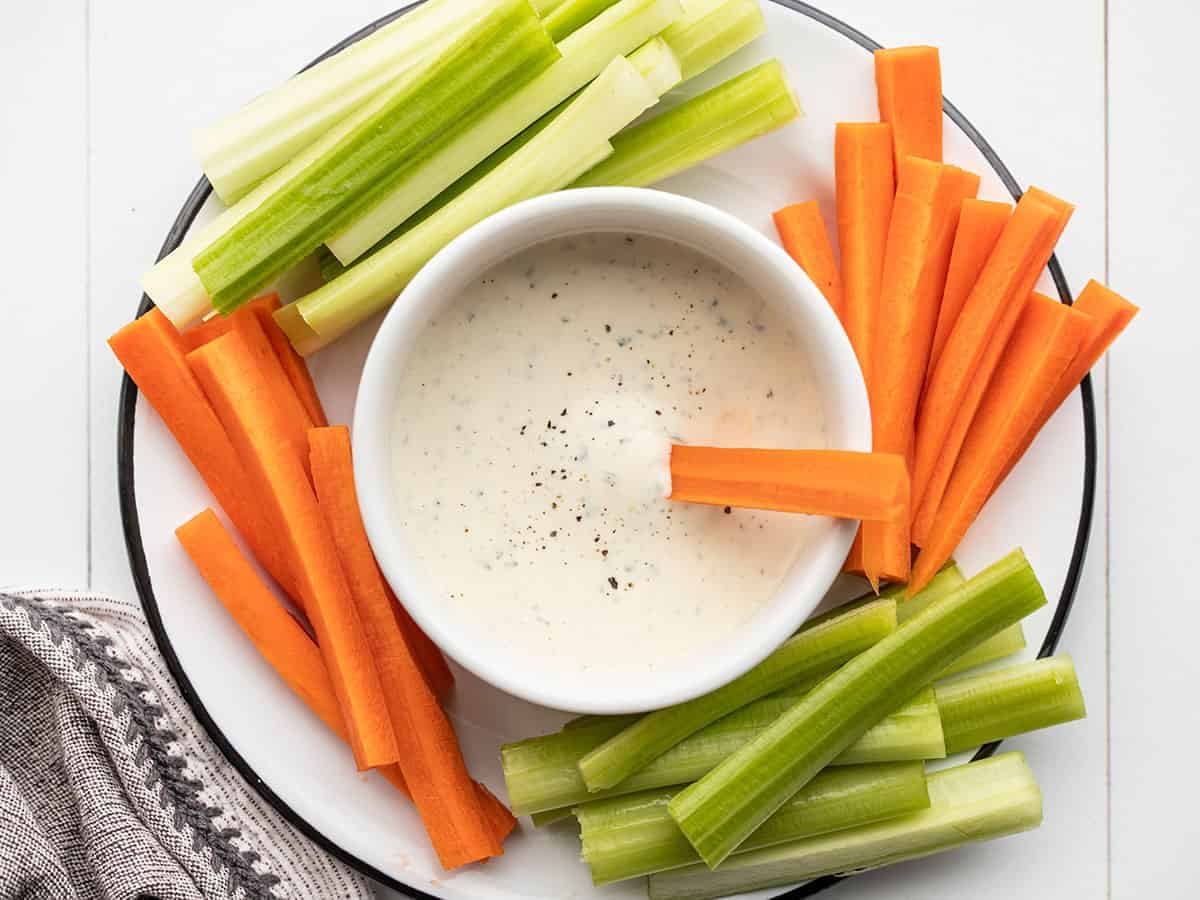 Ranch dressing in a bowl surrounded by carrots and celery