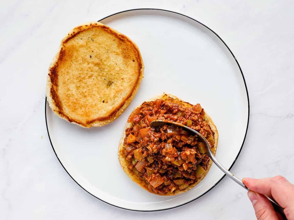Sloppy joe meat being spooned onto a toasted bun.