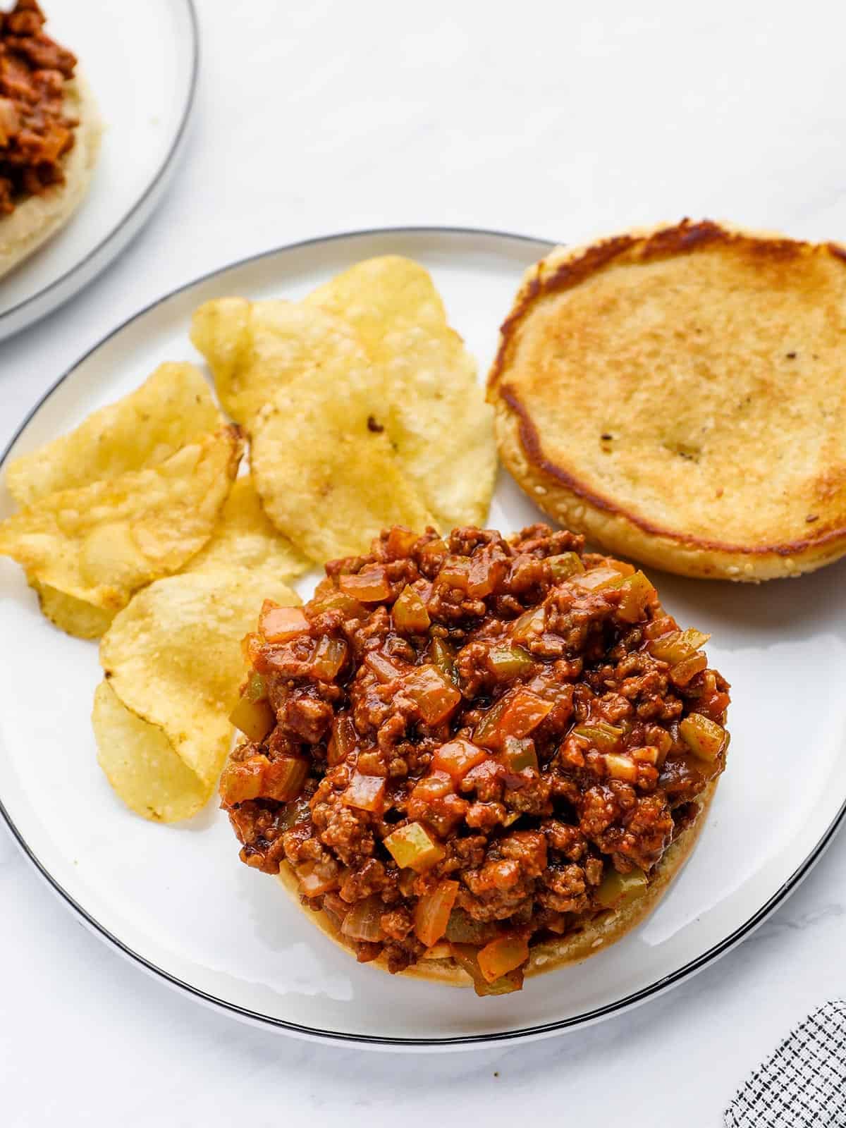 Open-faced sloppy joe on a plate with potato chips.
