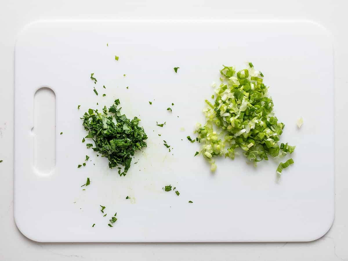 Chopped parsley and sliced green onion on a cutting board.