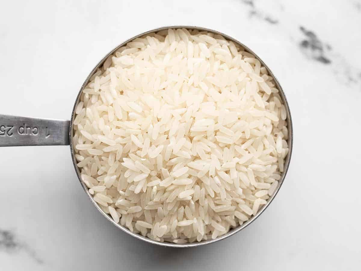 Uncooked rice in a metal measuring cup.