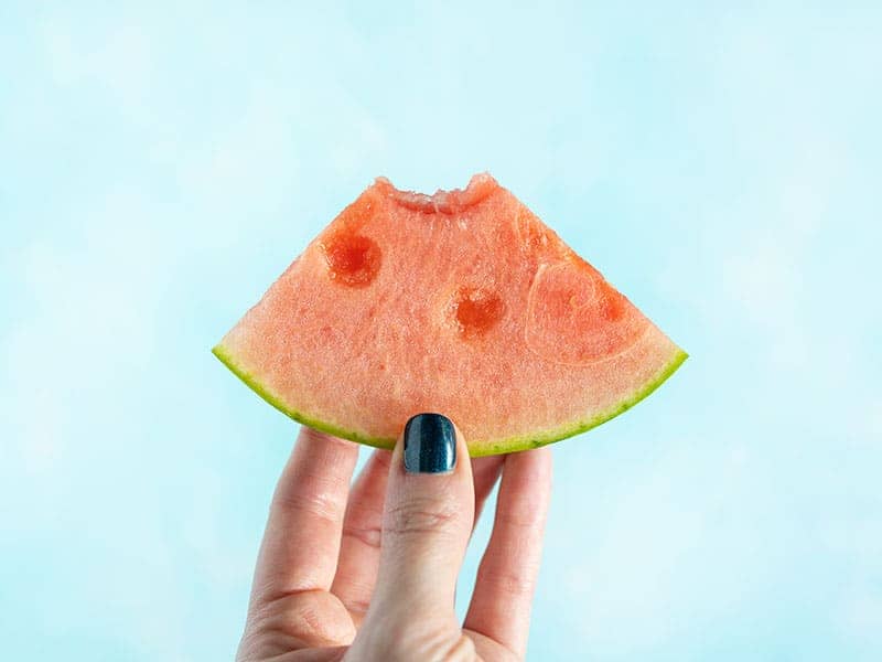 A hand holding a watermelon wedge with one bite taken out