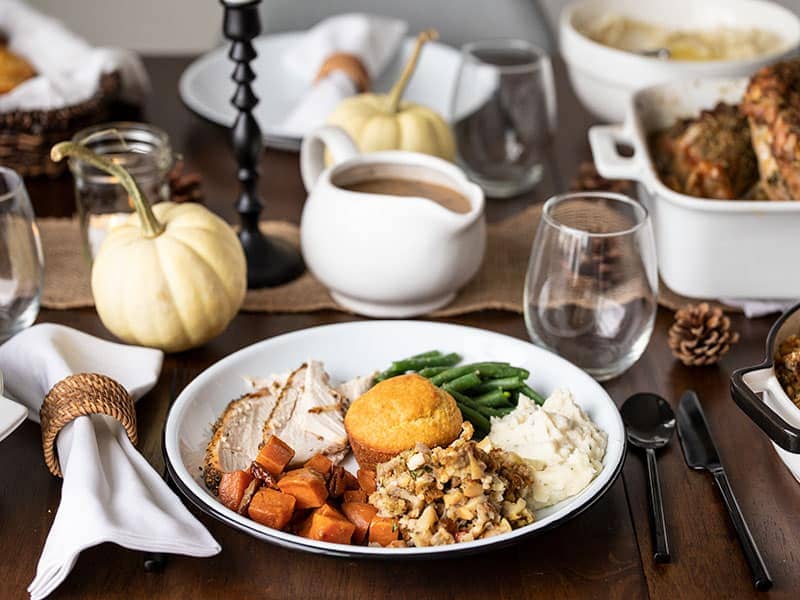 Close up view of a full Thanksgiving dinner plate with other dishes on the table in the background