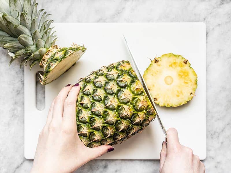 A pineapple on a white cutting board with the top and bottoms cut off.