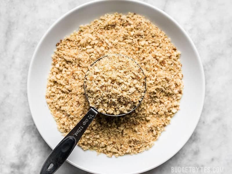 Breadcrumbs in a bowl with a measuring cup scooping some