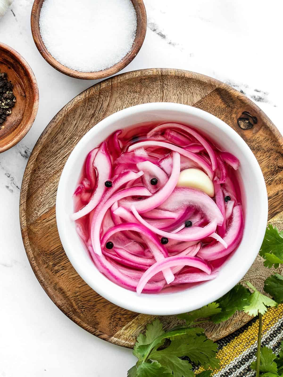 Overhead view of a bowl of pickled red onions on a wooden plate with wooden bowls on the side