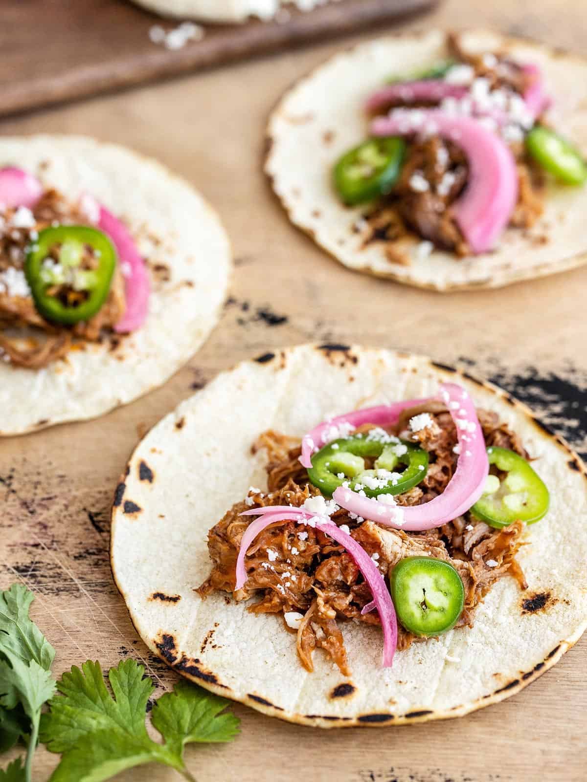 Three pulled pork tacos with pickled red onions and jalapeños.