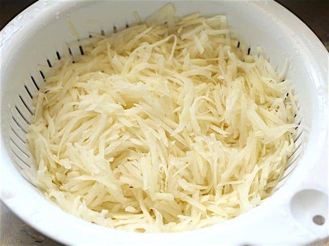 Shredded potatoes in strainer to rinse 
