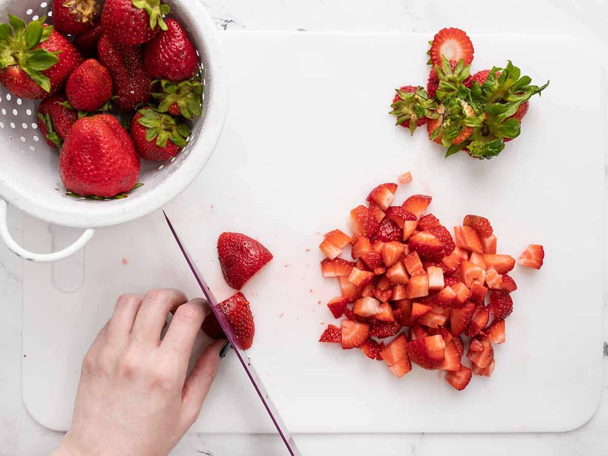 Strawberries being chopped on a cutting board.