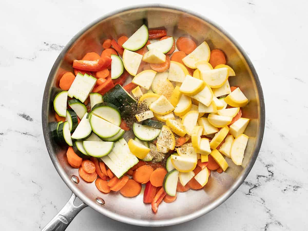 Zucchini, squash, bell pepper, and herbs added to the skillet