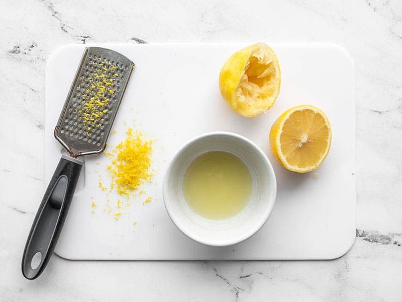 A zested and juiced lemon on a cutting board
