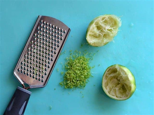 Juiced and zested lime on a blue cutting board next to a fine holed cheese grater