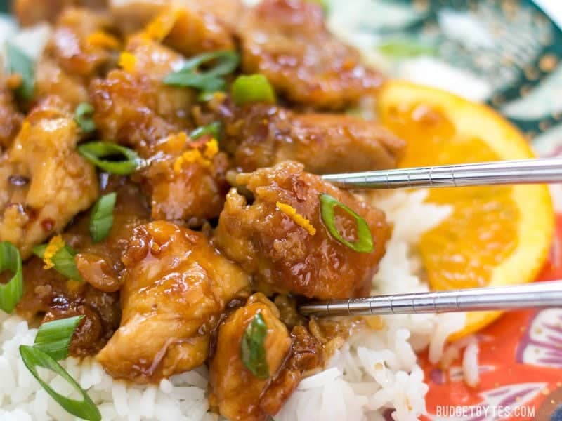 close up of a chunk of orange chicken being picked up by a pair of chopsticks 