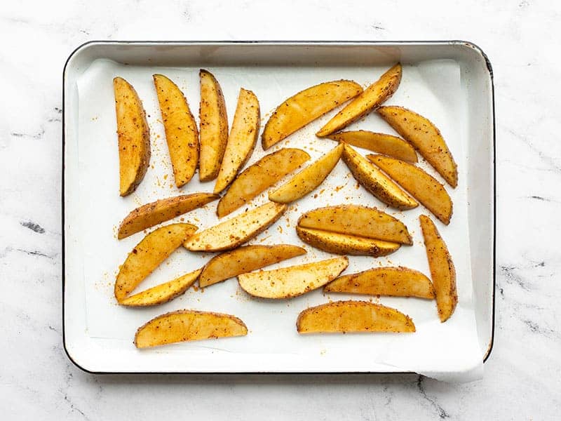 Potato wedges spread out on the parchment lined baking sheet