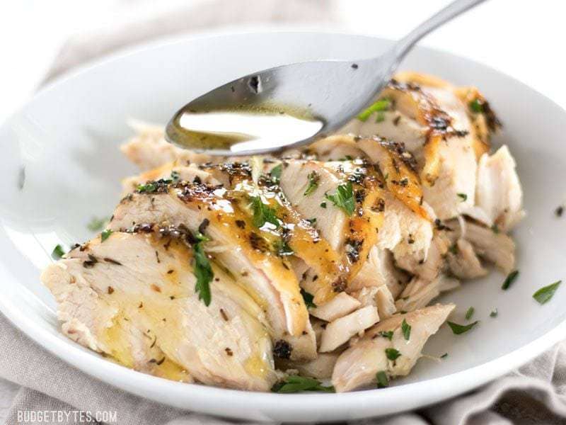Juices being spooned over sliced Herb Roasted Chicken Breast in a bowl