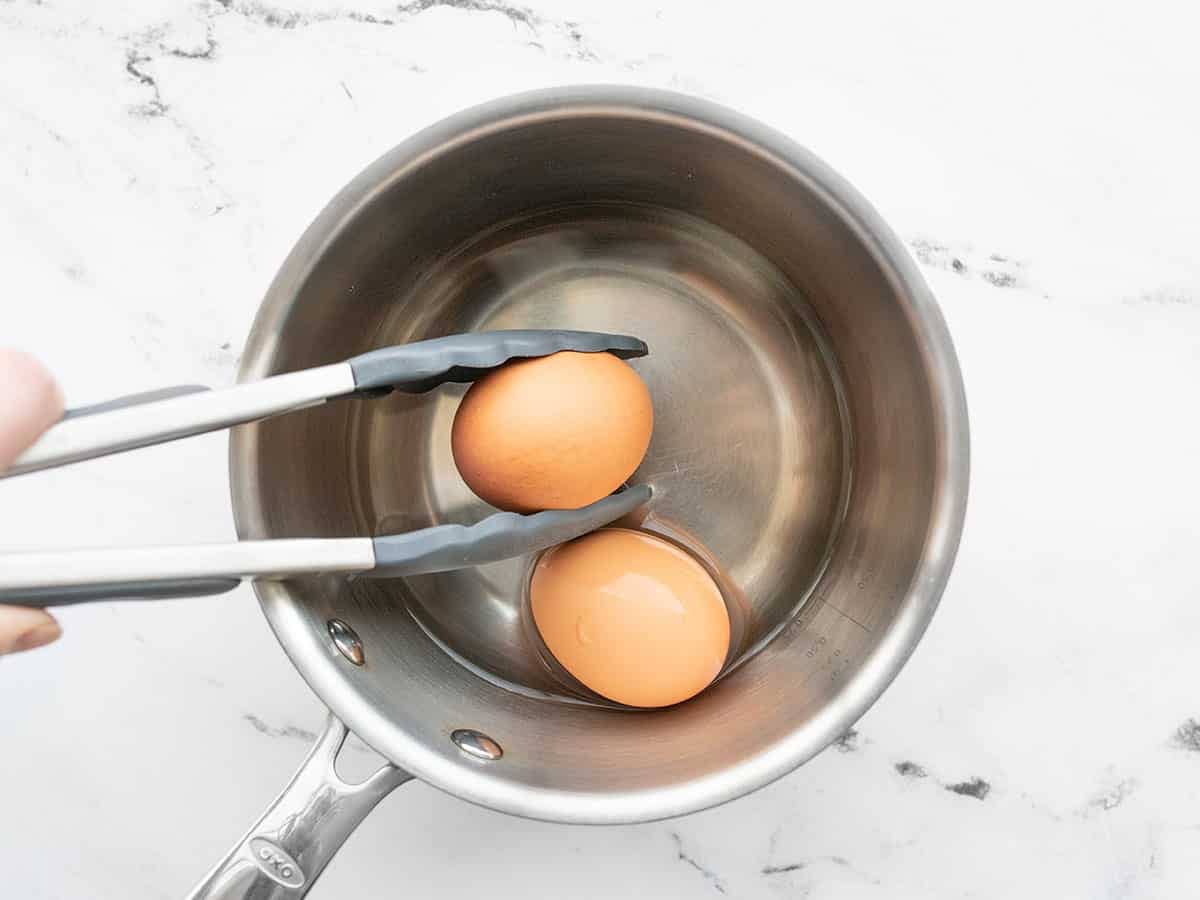 Eggs being added to a saucepot with tongs