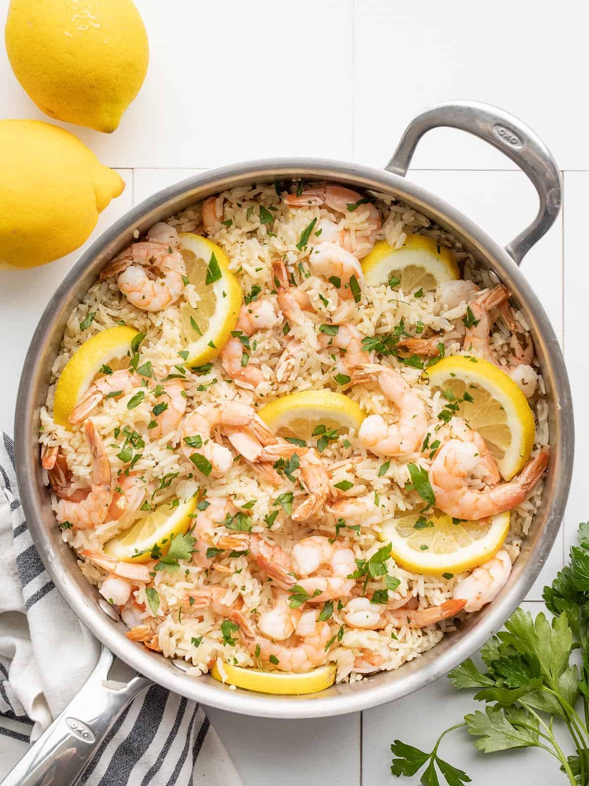 lemon garlic shrimp and rice in a skillet with lemons and parsley on the sides