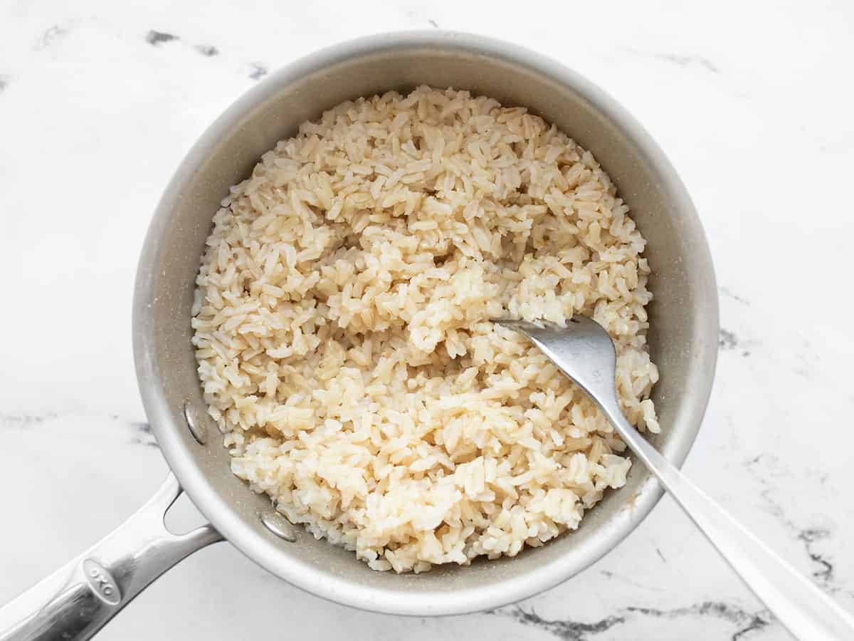 Cooked brown rice in a pot being fluffed with a fork