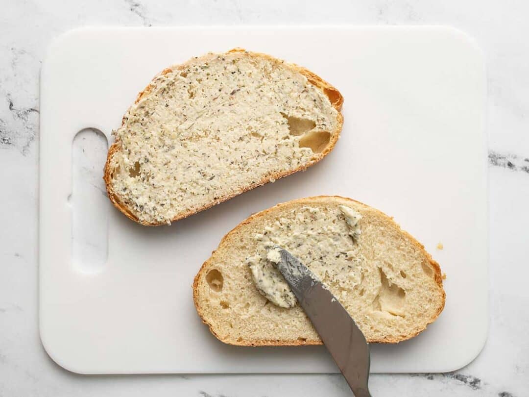 Knife spreading parmesan butter on bread.