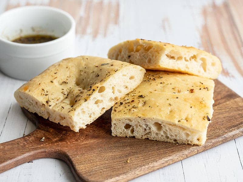 Three slices of no-knead focaccia piled on a wooden cutting board