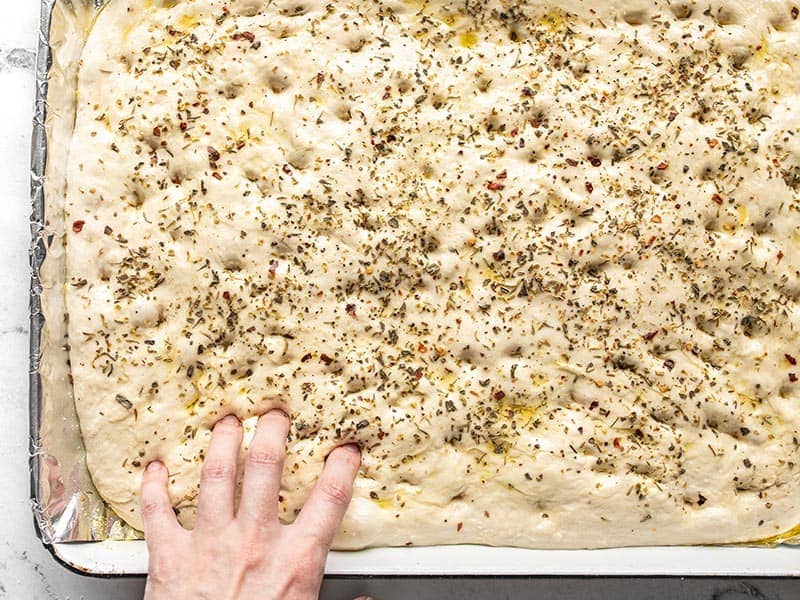Fingers making indentations in unbaked focaccia