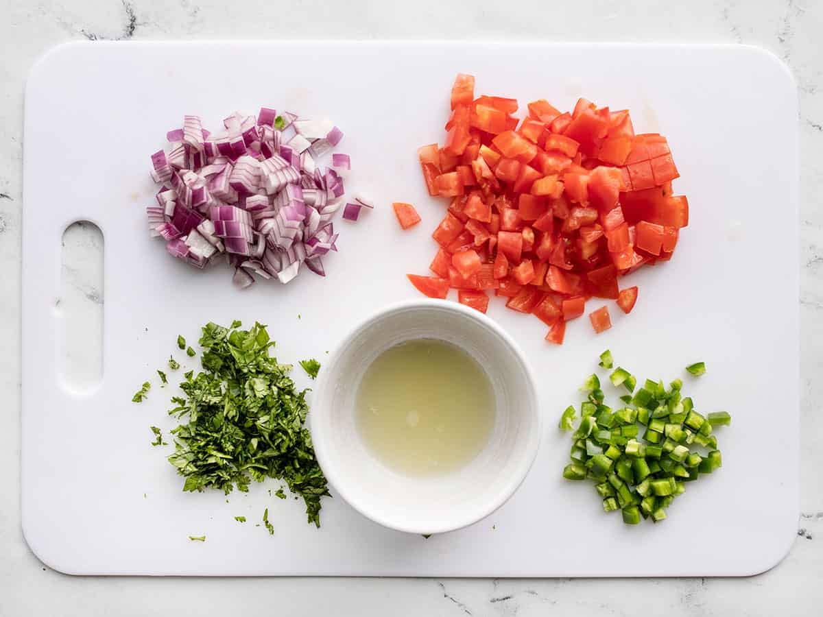 Chopped vegetables on a cutting board with a bowl of lime juice.