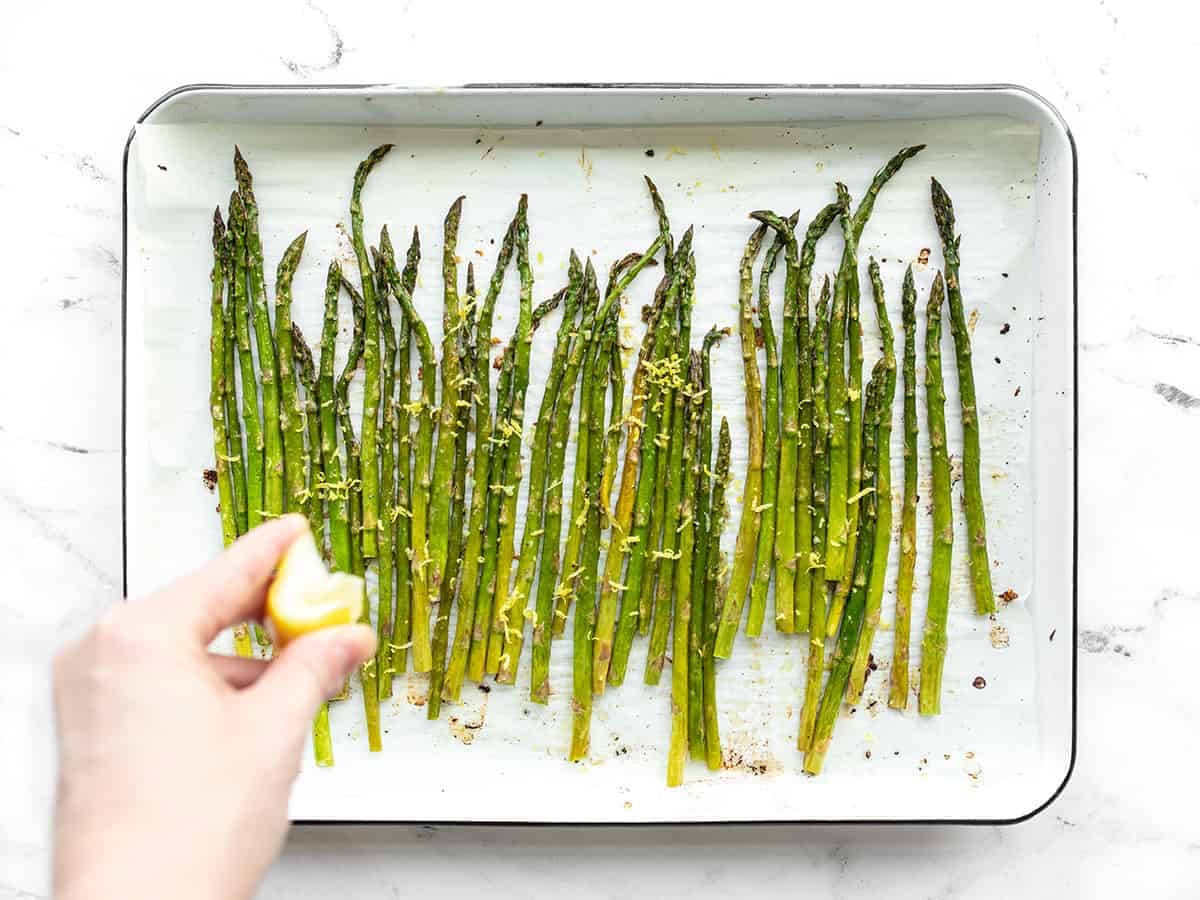 Lemon being squeezed on roasted asparagus