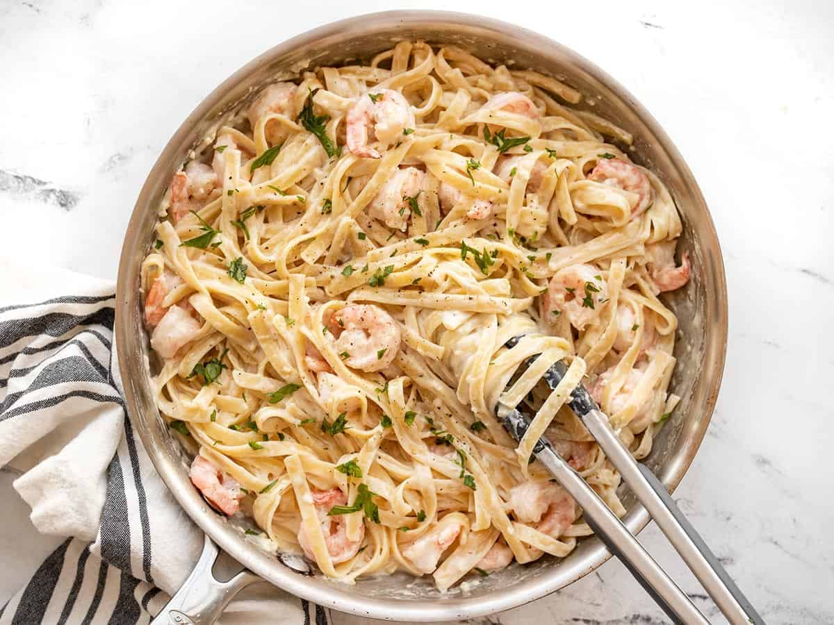 finished shrimp alfredo in the skillet with tongs