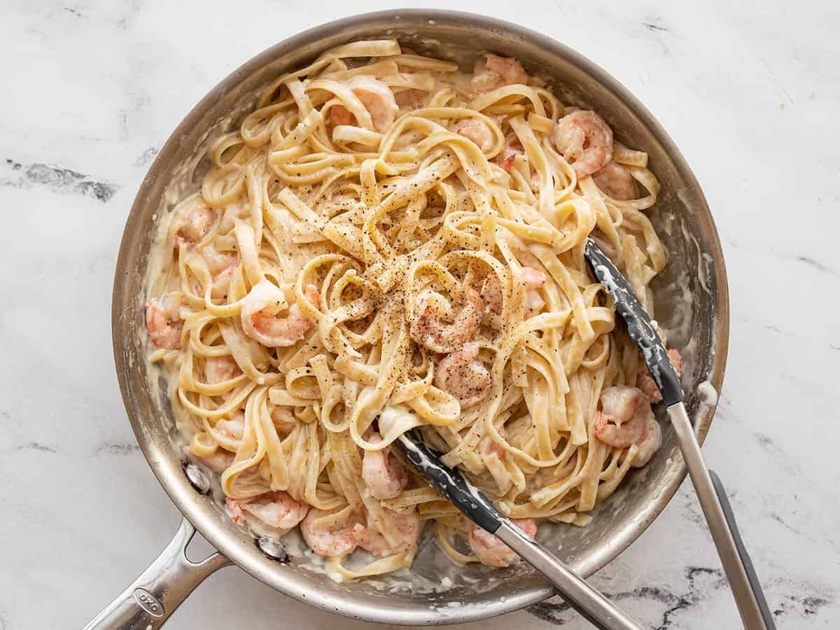 Pasta and shrimp tossed in the alfredo sauce with tongs on the side