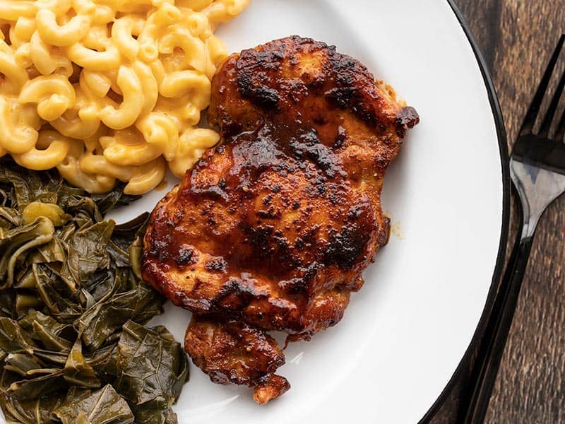 BBQ chicken thigh on a plate with mac and cheese and collard greens
