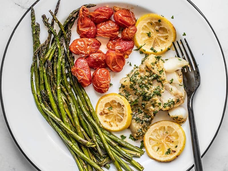 Overhead view of the plate full of tomatoes, asparagus, and Garlic Butter Baked Cod.