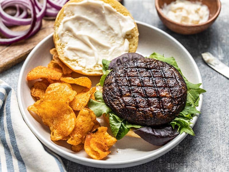 An open marinated portobello mushroom burger on a plate with chips, viewed from the front.