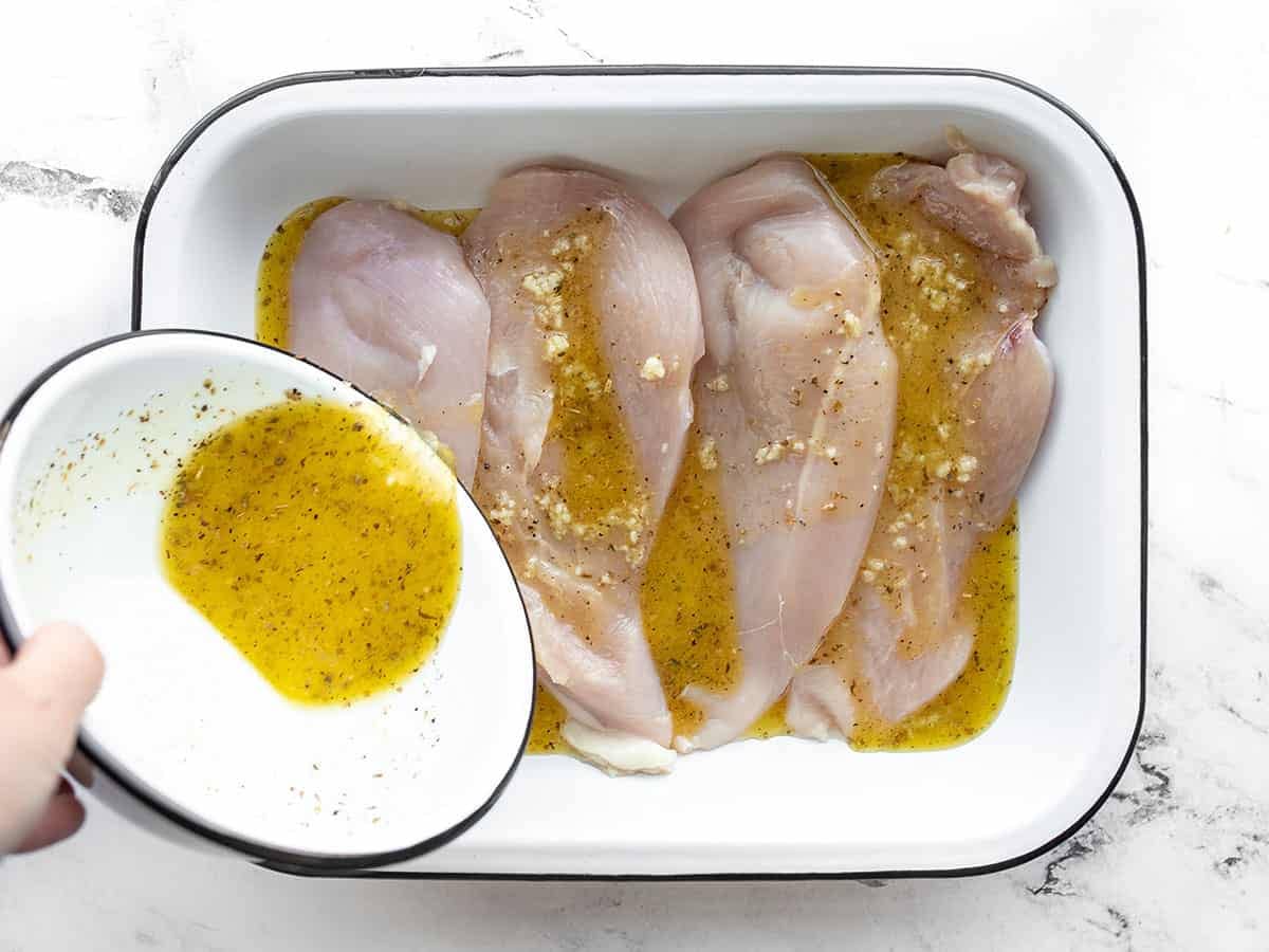 Marinade being poured over the chicken in a dish