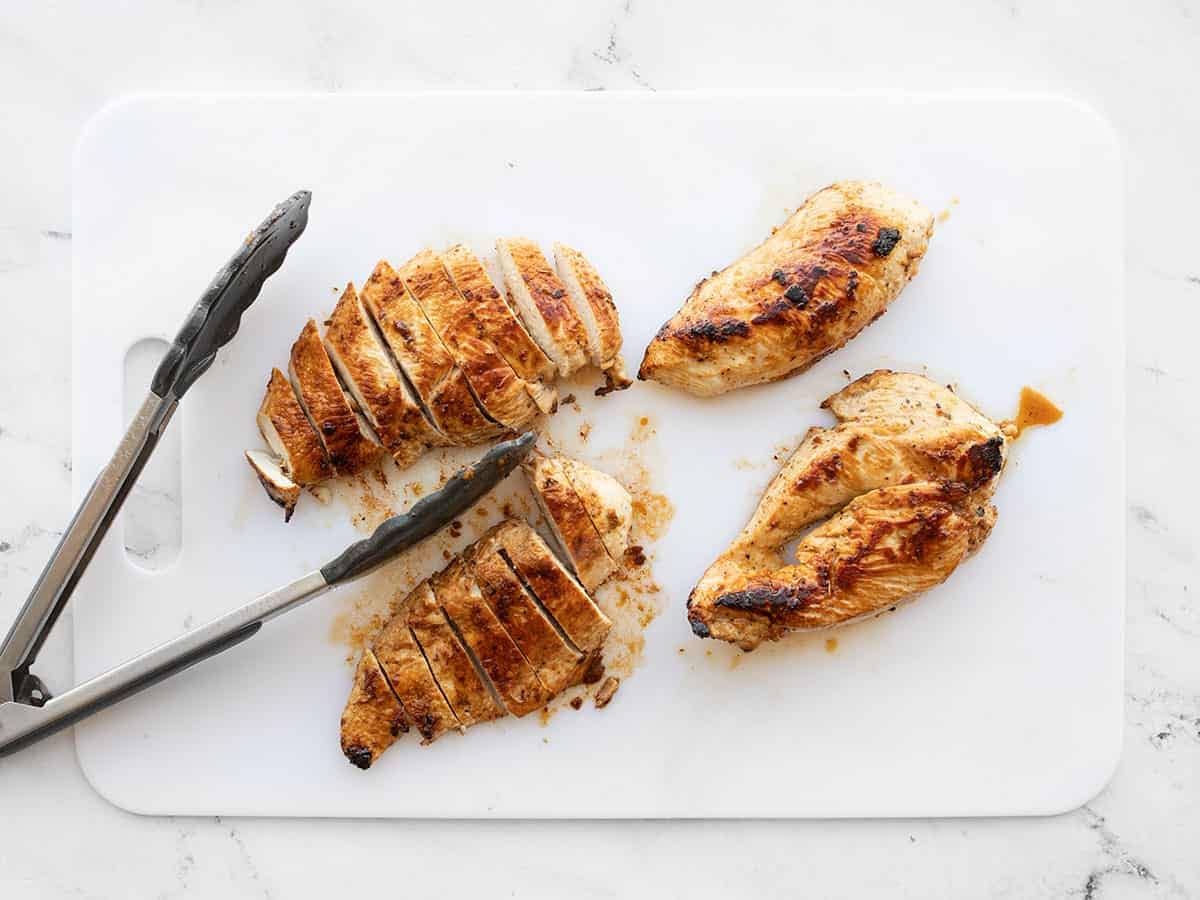 Sliced chicken on a cutting board with tongs