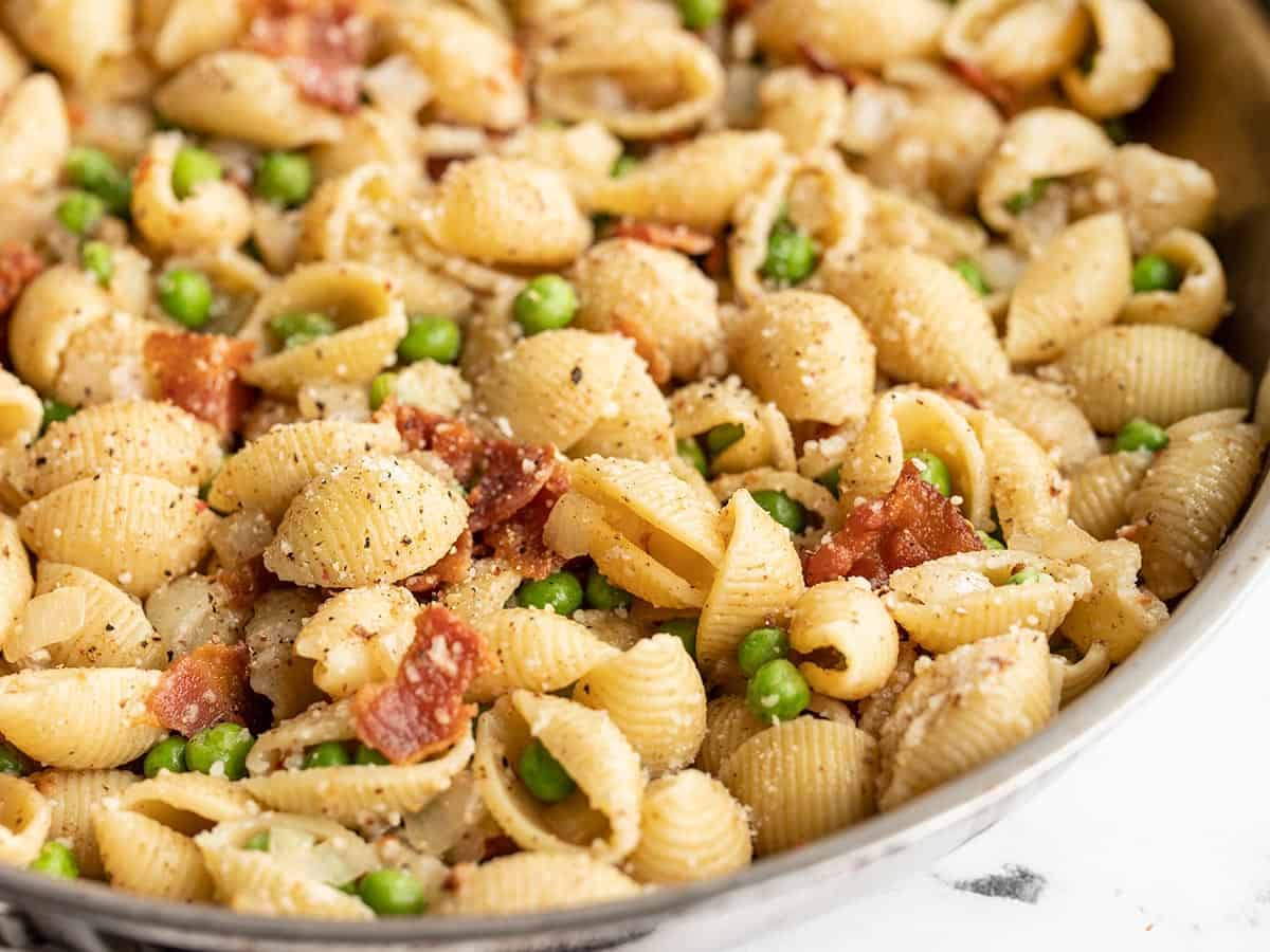 close up side view of pasta with bacon and peas in the skillet.