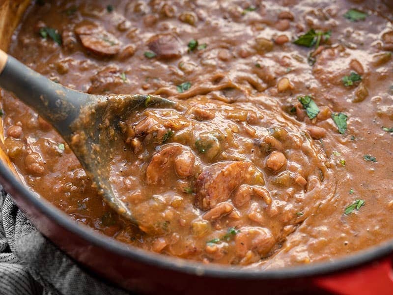 Close up of a spoon scooping some red beans and andouille sausage out of the pot