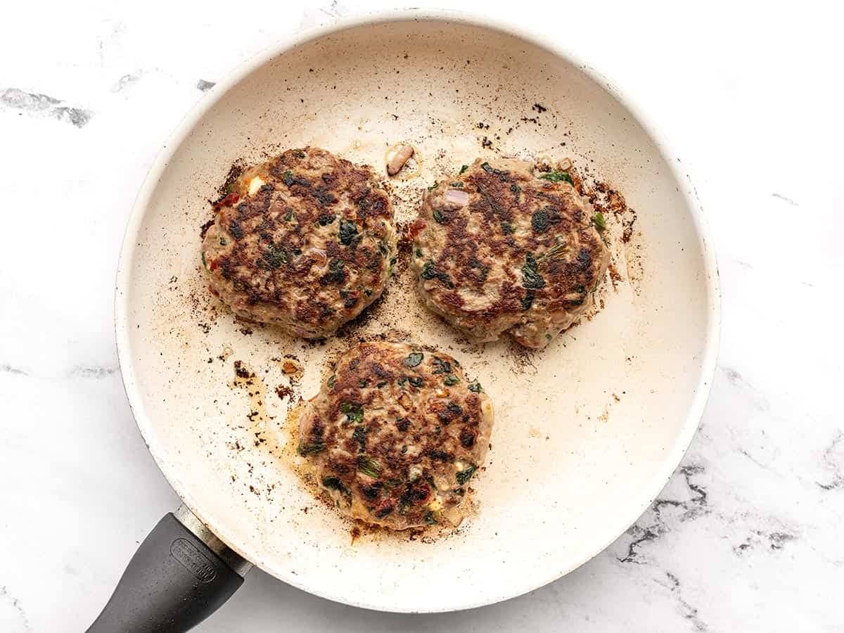 Three cooked turkey burgers in a skillet