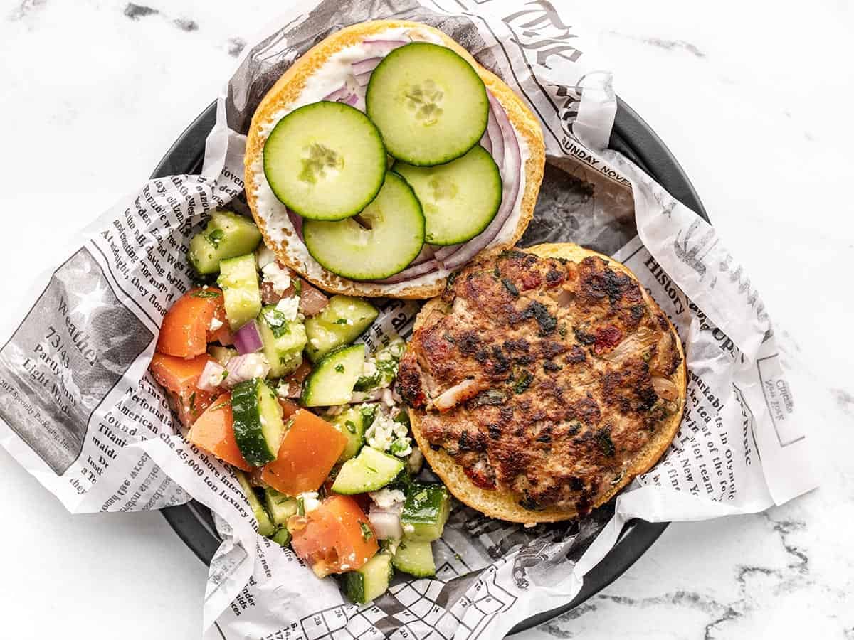 Overhead view of an open faced Mediterranean Turkey Burger on a paper lined plate with cucumber salad on the side