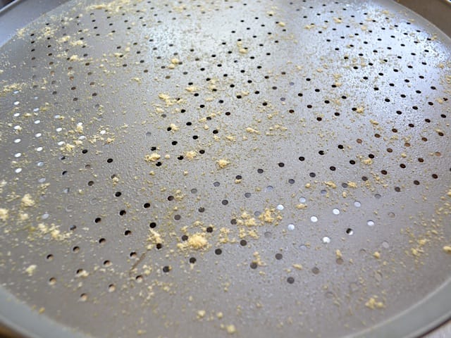 pizza pan covered with non stick spray and corn meal 