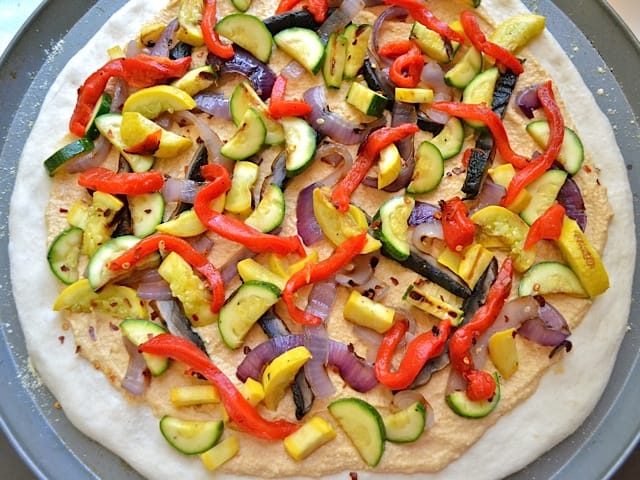 all ingredients (hummus and veggies) placed on pizza dough and ready to bake 
