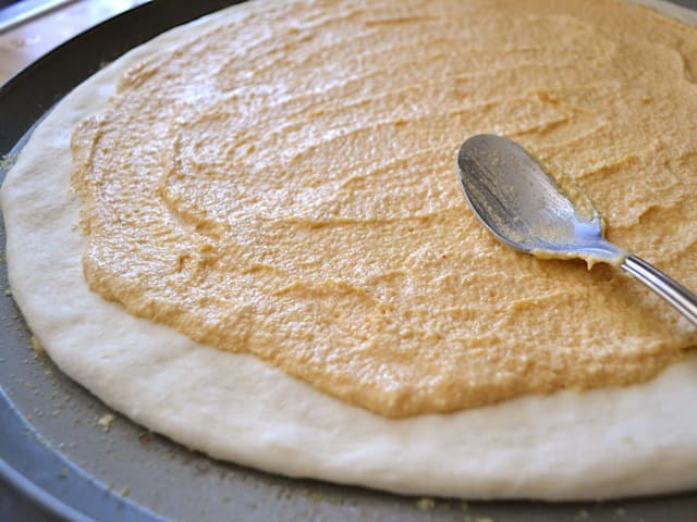 pizza dough on pizza pan with hummus spread on top 