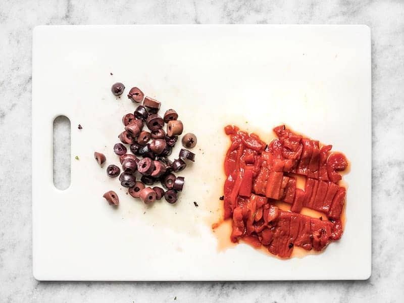 Chopped kalamata olives and roasted red peppers on the cutting board