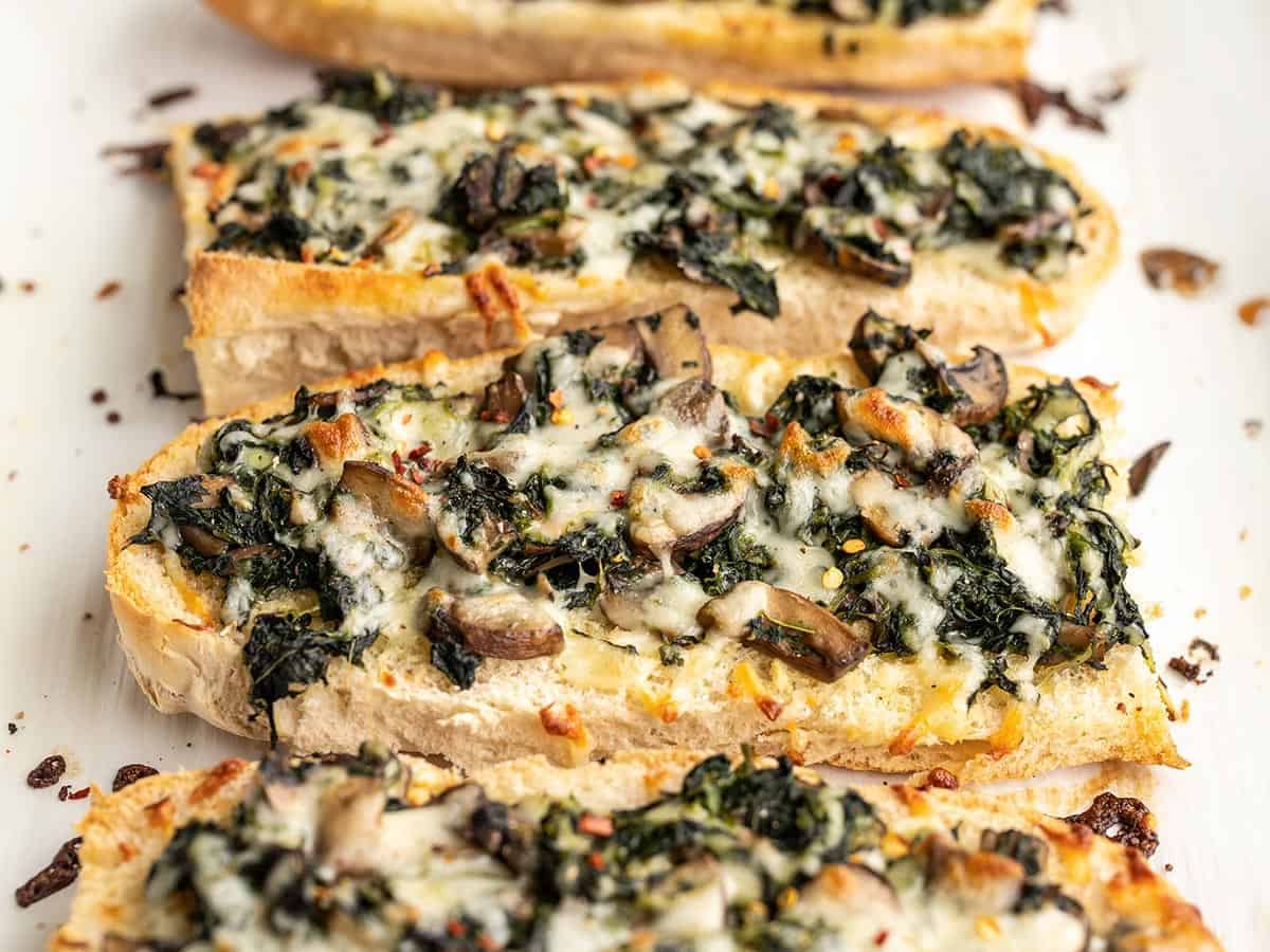 Side view of baked spinach mushroom French bread pizzas on the baking sheet.