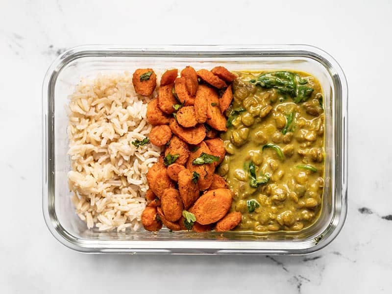 Creamy Coconut Curry Lentils in a glass meal prep container with rice and curry roasted carrots