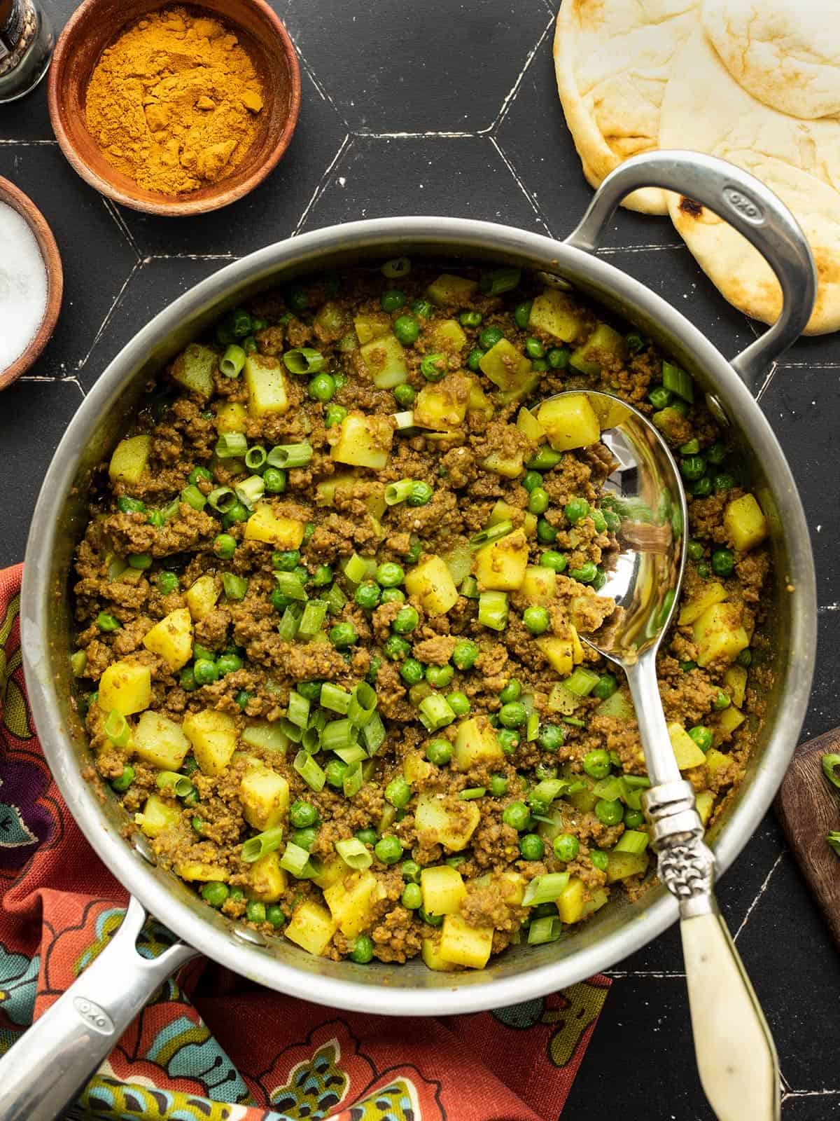curried ground beef with peas and potatoes in a skillet with a serving spoon