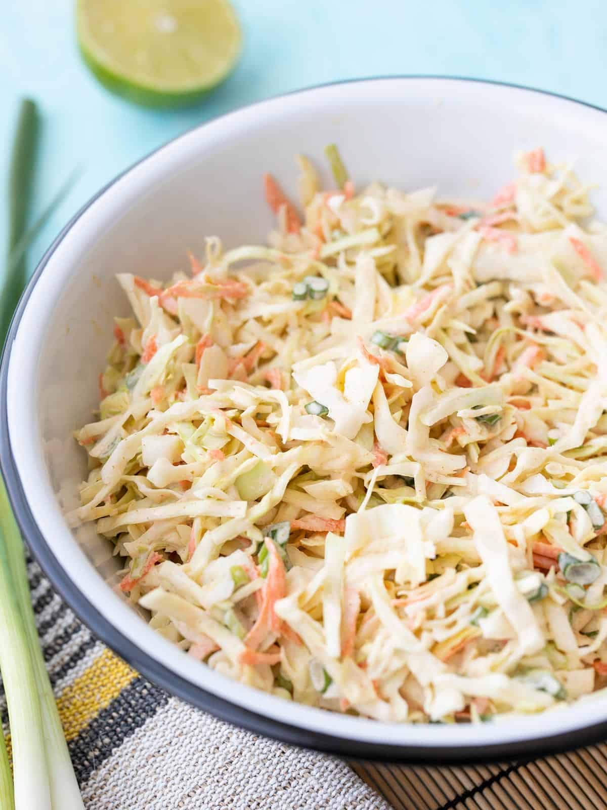 side view of a bowl of cumin lime coleslaw with green onion and limes on the side