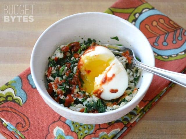 Soft boiled egg put on top of rice and spinach mixture in bowl 