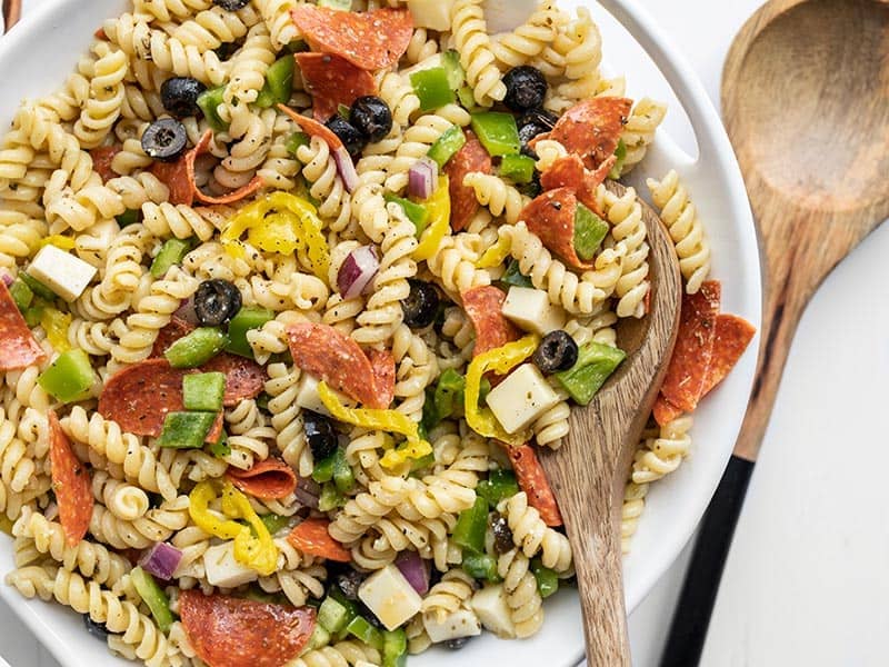 Close up of a serving bowl of pizza pasta salad, a wooden spoon in the side