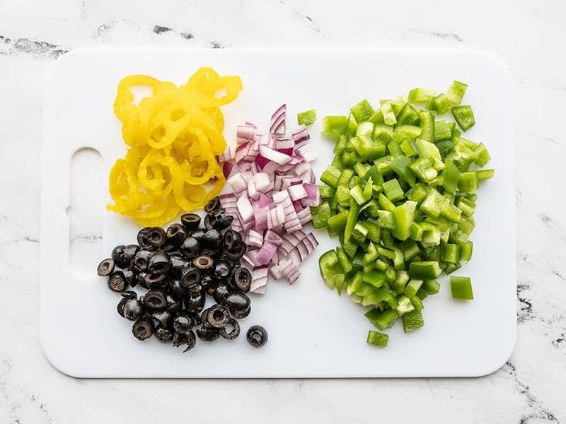 Bell pepper, red onion, black olives, and banana peppers on a cutting board